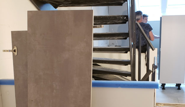 Mein Küchenatelier zeigt ein Bild von der Montage von Schränken einer Küche in betongrau hinter einer offenen Treppe