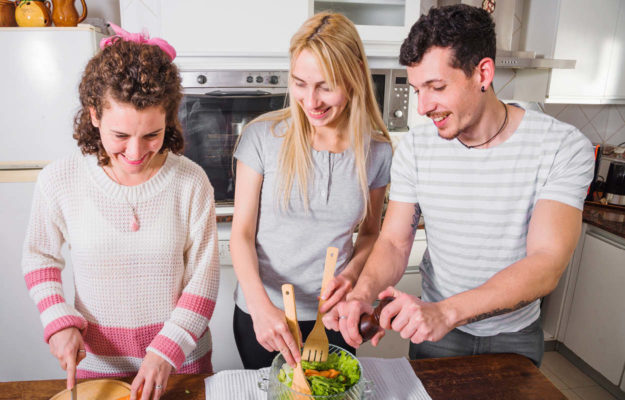 Drei Freunde bereiten gemeinsam einen Salat zu.